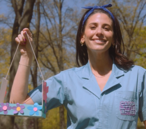 A woman with medium-length brown hair tied back in a bandana and collared shirt holding a bird feeder made from an empty box of Little Muffins.